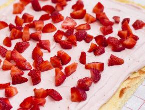 Joghurt-Sahnemischung und kleingeschnittene Erdbeeren auf dem Teig verteilt